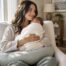 New mother holding her swaddled newborn on a nursing pillow at home in Newport Beach